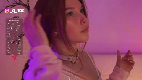Video of a young woman with light skin and straight brown hair, wearing a white top with a silver choker, holding a hairbrush under a pink-lit room, with social media icons overlayed.