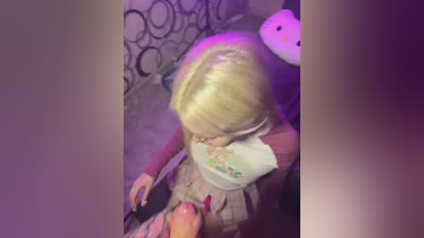 Media: A video shows a young blonde girl wearing a pink dress, playing with a stuffed toy on a circular-patterned carpet. The image is dimly lit with purple hues, giving it a dreamy, nostalgic feel.