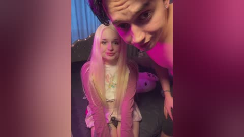 Media: Video of a young blonde girl in a pink jacket and white dress, leaning against a man with short black hair, in a dimly lit room with purple and blue lights.