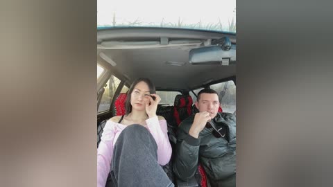 Media: Video of a young Asian woman and man in a car, both wearing casual attire. The man is holding a phone, while the woman has her hand on her forehead, looking tired.