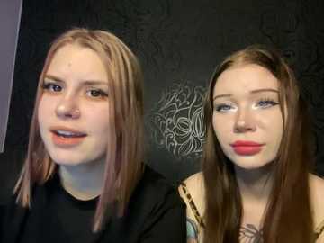 Media: Video of two young women with light skin, long brown hair, and full makeup, standing side by side against a dark, ornate wallpaper. One wears a black top, the other a leopard print blouse.