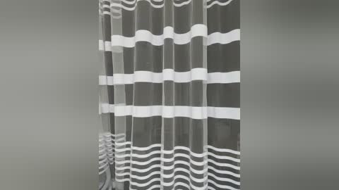 Video of a gray curtain with white wavy stripes, hung against a plain, light gray wall, creating a simple and modern aesthetic.