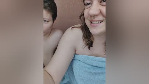 Media: Video of a young couple in a bathroom; the man, shirtless, has short brown hair, while the woman, with shoulder-length brown hair, wears a towel. They smile, creating a warm, intimate atmosphere.