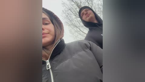 Media: Video of two young people wearing winter jackets, smiling, taken from a low angle. The background shows bare trees, suggesting a cold, wintry day.