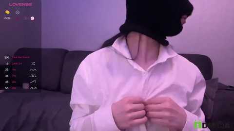 Video of a person with a black mask and white shirt, viewed from behind, in a dimly lit room.