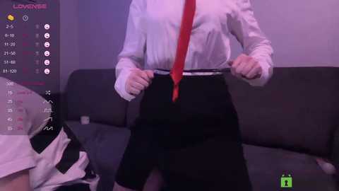 Video of a person in a white dress shirt with red tie, black skirt, adjusting belt, in a dimly lit room with a calendar and clock visible.