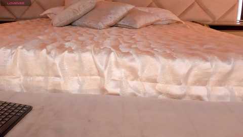 Video of a luxurious bedroom featuring a plush, cream-colored bed with a quilted duvet and matching pillows, set against a tufted, padded headboard. The room exudes a warm, inviting ambiance with soft lighting.