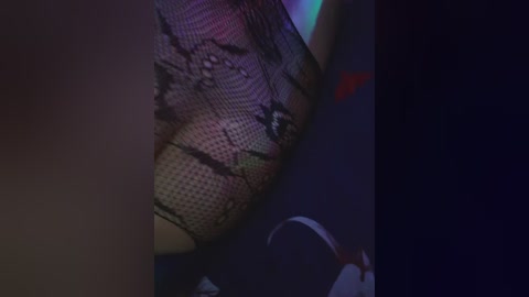 A dimly-lit video shows a close-up of a woman's leg in fishnet stockings, partially obscured by a shadowy figure. The background is dark, with faint neon colors suggesting a nightclub setting.