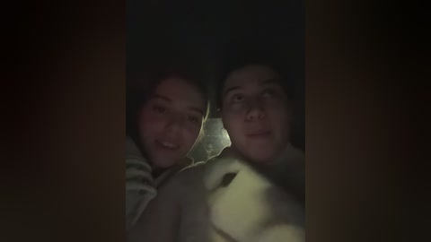 Media: Video of two young Asian women smiling, their faces partially obscured by a dark curtain. The image is dimly lit, creating a cozy, intimate atmosphere.