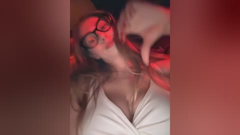 Media: A blurry, dimly lit video of a woman with glasses, fair skin, and a white top, partially obscured by a hand.