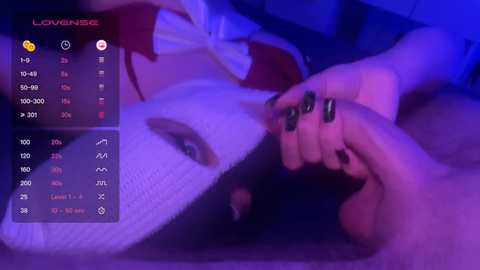 Video of a young woman with light skin, wearing a white lace bra and red bow, lying on a bed, with a man's hand holding hers, in a dimly lit, purple-hued room, displaying a \"Lovense\" virtual reality interface.