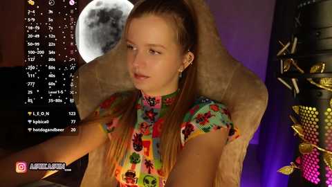 Video of a young woman with light skin and straight brown hair in a high ponytail, wearing a colorful floral top, seated in a plush chair. Moon and starry night background. Streaming overlay.