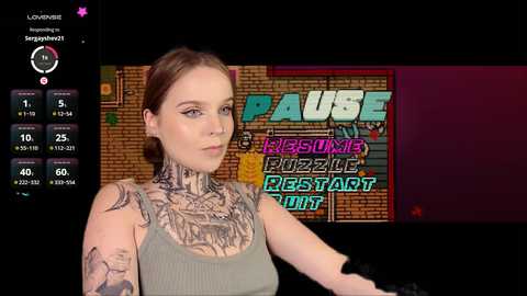 Media: A video of a tattooed woman with fair skin and brown hair, wearing a gray tank top, standing in front of a brick wall with a \"Puzzle Party\" sign.