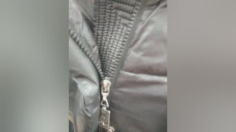 Video of a black, textured, zippered jacket with a shiny, reflective surface, prominently displaying the metallic zipper pull and detailing.
