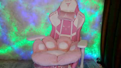 A video of a pink gaming chair with a plush, cushioned seat, set against a backdrop of vibrant, multicolored LED lights. The chair features a large, furry paw print on the seat.