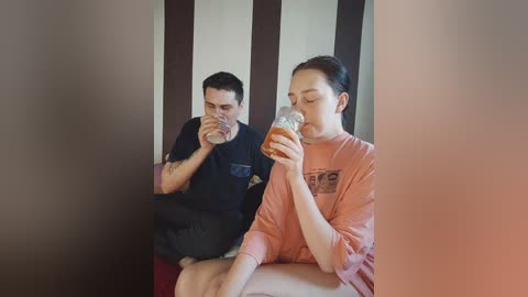 Video of a man and woman seated at a table, both drinking beer, the woman wearing a \"Star Wars\" t-shirt, in a dimly lit room with vertical dark wood paneling.