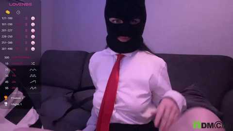 A video of a person in a black balaclava, white shirt, and red tie, reclining on a gray couch, with a \"LOVIN' IT\" screen overlay and a \"DMG\" watermark.