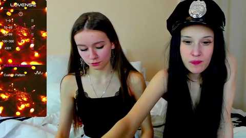 Media: Video of two young women, one in a black dress, the other in a cop hat, indoors with a blurred cityscape background.