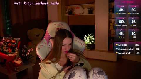 Media: Video of a young woman with long brown hair, wearing a plush \"Kusha\" headband, sitting in a dimly lit room. She holds a phone, displaying a chat window with various messages.