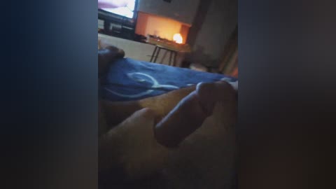 A dimly lit video of a person lying on a bed with a large, erect penis visible, in a room with a TV screen and warm lighting.