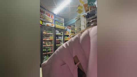 Media: Video of a dimly-lit convenience store interior, showing a person in a white coat standing near the entrance, with brightly lit shelves of assorted products in the background.