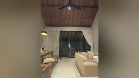 Media: Video of a minimalist living room with beige sofa, wooden ceiling, and large windows with sheer white curtains.