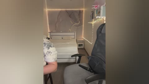 Media: A video of a dimly lit, cozy bedroom with string lights, a white bed, a black chair, and a person partially visible wearing a white shirt.