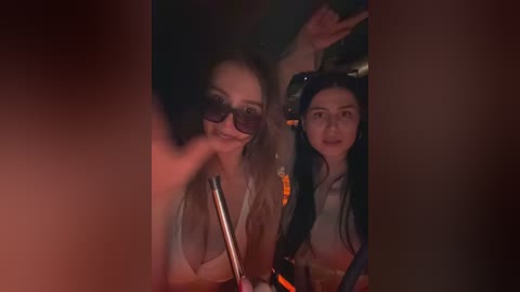 Media: Video of two women, one with long blonde hair, the other with dark hair, both wearing headsets, sitting in a dimly lit car at night.