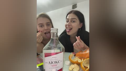 Media: Video of two young women, one with long blonde hair, the other with dark hair, sticking out their tongues, seated at a table with a bottle of Absolut vodka, orange slices, and Halloween pumpkins.