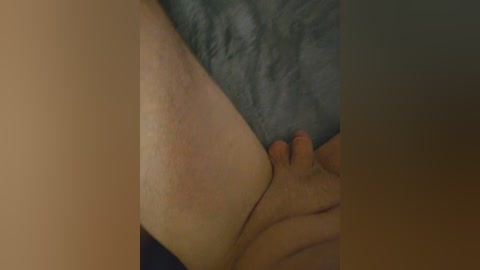 A close-up video of a light-skinned person's hand gently touching the inner thigh of another person, whose skin is slightly darker. The background is blurred with a hint of a dark, possibly gray, fabric.