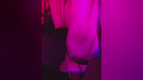 Video with a purple and pink hue, showing a person in a white shirt, partially visible, standing in a dimly lit room.