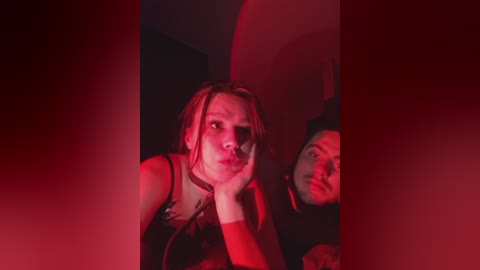Video of a woman with shoulder-length blonde hair, wearing a black dress, leaning on her hands, bathed in red light.