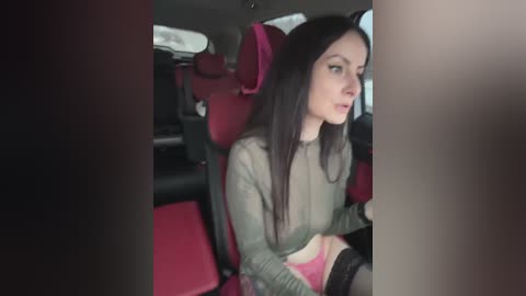 Media: Video of a young woman with long dark hair in a green sweater, sitting in a red car seat, partially obscured by a man's hand.