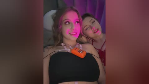Media: Video of two young women in a dimly lit room, one with a black bra, the other leaning on her shoulder.