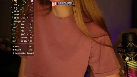 Video of a woman with long blonde hair in a pink top, standing in front of a microphone, with a streaming interface overlay.