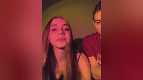 Video of a young Caucasian woman with long, straight hair and a small nose, wearing a sleeveless top, standing next to a man with short dark hair, partially obscured by a vertical red filter.