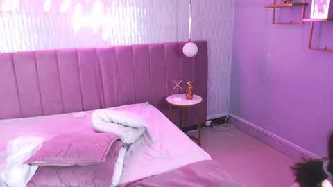 Video of a modern, minimalist bedroom with a light purple color scheme. The bed features a tufted, upholstered headboard and is neatly made with white linens and a gray throw blanket. A small round wooden nightstand holds a decorative vase. The walls are adorned with vertical white paneling and a hanging pendant light.