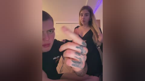 Media: Video of a young woman with blonde hair in a black dress and a man with a shaved head in a black shirt, both in a dimly lit room with purple LED strip lights.