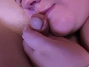 Media: Video of a close-up, intimate moment showing a penis being sucked by a person with light skin and a partial glimpse of their face. The lighting is dim, casting a soft pink hue.