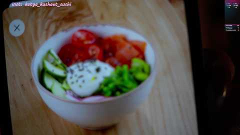 Media: Video of a white bowl on a wooden surface, containing vibrant ingredients like green leaves, red tomatoes, yellow avocado, and white quinoa, with a pinkish background.