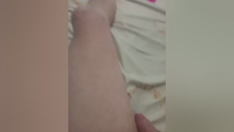 A close-up video of a fair-skinned person's thigh, partially covered by a white sheet with floral patterns. The image is slightly out of focus, making it difficult to discern details clearly.