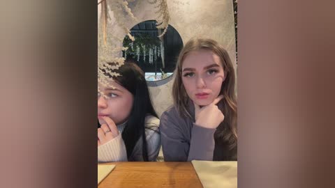 Media: Video of two young women with fair skin and long hair, one with dark hair, the other with light brown hair, in a dimly lit, rustic setting.