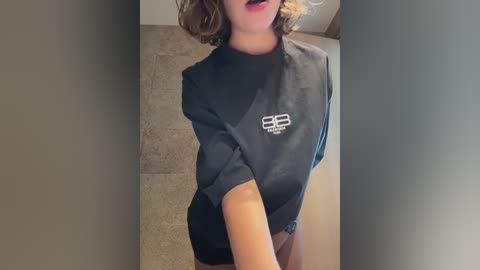 Media: A video of a person with fair skin and wavy brown hair, wearing a black BCBG dress and red lipstick, standing in a beige-tiled bathroom.