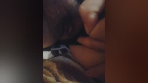 A close-up video of a dark-skinned person with a full beard, lying face-down on a bed with a patterned blanket, in a dimly lit room.