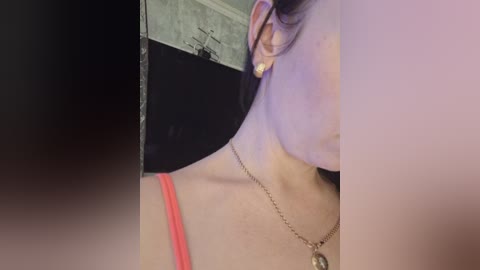A close-up video of a woman's profile, with her left ear and part of her neck visible. She wears a red bra and a delicate gold necklace. Her skin is light, and she has a faint purple hue on her neck.