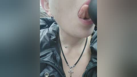 Video of a fair-skinned, young woman with pale lips, tongue extended, wearing a black leather jacket and a black choker necklace. Her face is partially obscured by the camera's lens.