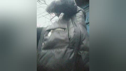 A blurry video of a person wearing a dark jacket, with a hood partially pulled up, standing in a dimly lit, urban setting.