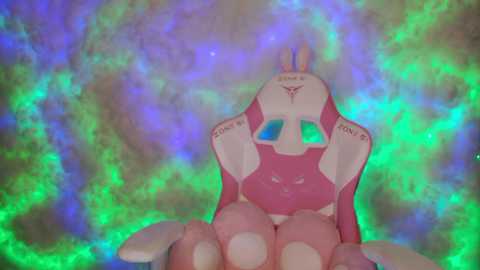 A CGI rendering of a pink, cartoonish robot with a smiling face and glowing blue eyes, seated on a green and purple nebula background. The robot has a futuristic design with \"M\" and \"M\" inscriptions on its shoulders.