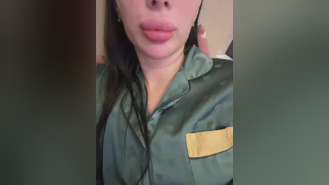 Video of a woman with fair skin, wearing a green military-style jacket with yellow patches, licking her lips, and partially visible long black hair.