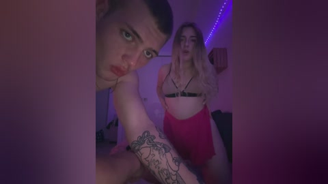 Media: Video of a young man with short hair, tattoos on his arm, and a woman with long hair in a dimly lit room.